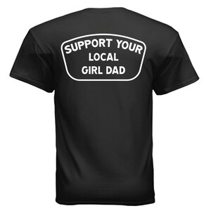 May include: Black t-shirt with the text "SUPPORT YOUR LOCAL GIRL DAD" in a white, rounded rectangle. The text is in a bold, sans-serif font. The shirt is a classic crew neck style.