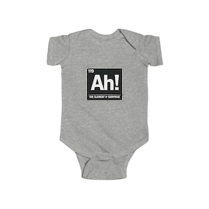 May include: A gray baby bodysuit with a black and white graphic that reads "Ah!" with the number "119" above it and "THE ELEMENT OF SURPRISE" below it. The bodysuit is made of a soft material.