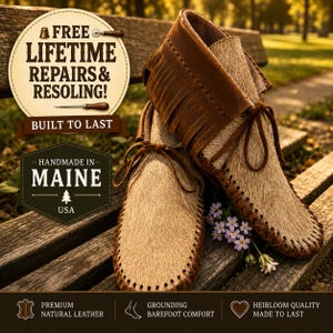 May include: Handmade in Maine, these moccasin-style boots feature a light brown, textured upper with dark brown leather trim and fringe. The boots have a stitched design and are tied with a leather cord. The image includes text that says "Free Lifetime Repairs & Resoling!"