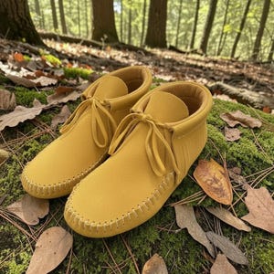 Puede incluir: Un par de mocasines de color amarillo mostaza que llegan al tobillo, con una textura suave similar a la gamuza, puntera redondeada con costuras visibles en el borde y cordones finos a juego atados con un lazo y flecos laterales.