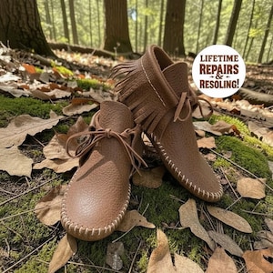 Puede incluir: Un par de mocasines de cuero marr&oacute;n con flecos, cordones finos y costuras blancas visibles en los bordes. Una pegatina blanca circular est&aacute; adherida a la imagen con el texto: LIFETIME REPAIRS & RESOLING!