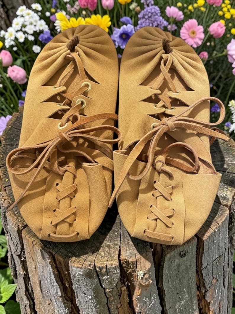 May include: A pair of tan leather moccasin-style slippers with lace-up detailing. The slippers have a soft, rounded toe and are tied with leather laces. The background features colorful flowers.