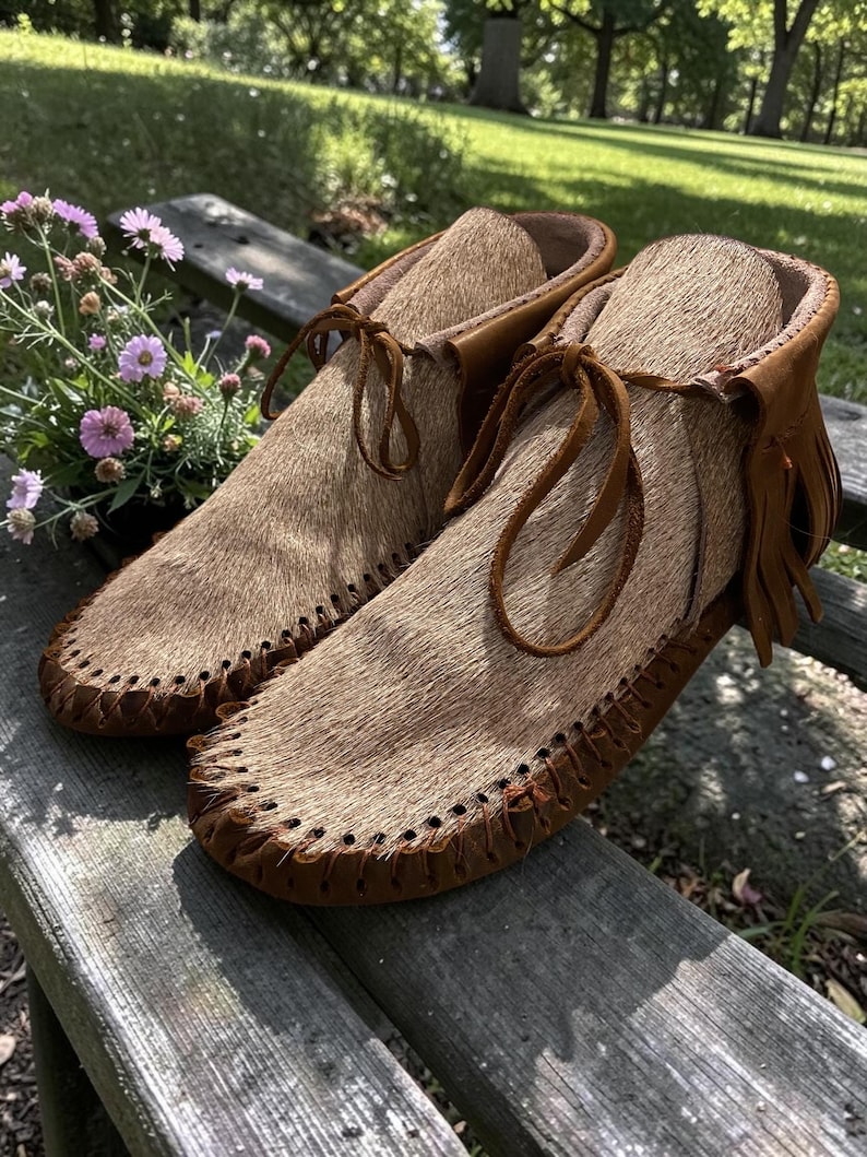 Puede incluir: Un par de mocasines de color tostado con una parte superior de piel texturizada, ribetes de cuero marr&oacute;n, detalles de costura en la puntera y cordones de cuero finos atados en la parte delantera. Los zapatos incluyen flecos decorativos en el tal&oacute;n.
