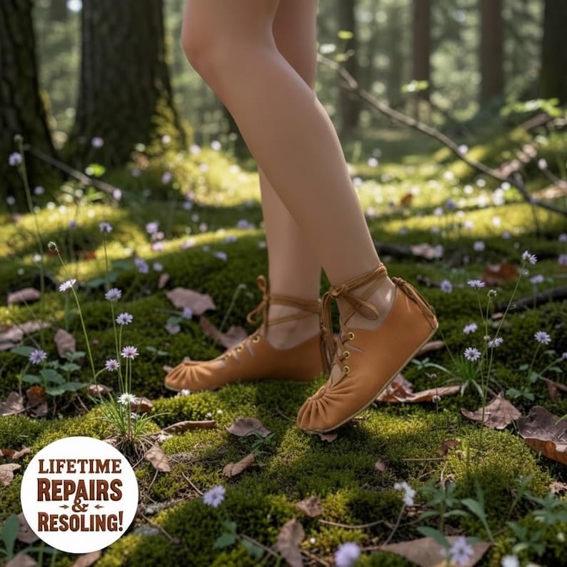 May include: A pair of tan leather ankle boots with laces, worn in a forest setting. The boots have a rounded toe and are tied with laces around the ankle. The image also includes the text "LIFETIME REPAIRS & RESOLING!"