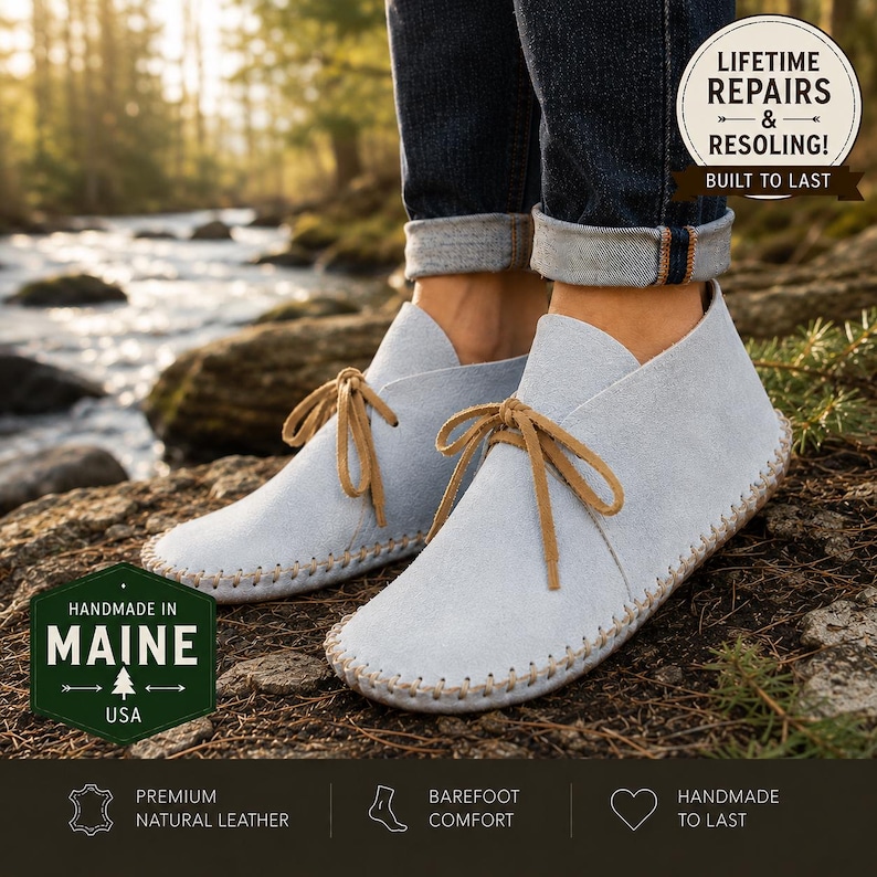 May include: Light blue suede ankle boots with tan leather laces and visible whipstitch detailing along the sole. The boots feature a soft, flexible construction and are worn with dark blue cuffed denim jeans. Text overlays include "LIFETIME REPAIRS & RESOLING! BUILT TO LAST" and "HANDMADE IN MAINE USA".