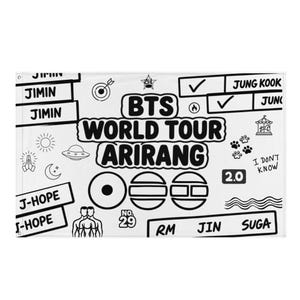 Puede incluir: Una bandera en blanco y negro con el texto "BTS WORLD TOUR ARIRANG" y varios garabatos. El diseño incluye nombres de miembros de la banda, marcas de verificación, huellas de patas y otros símbolos.