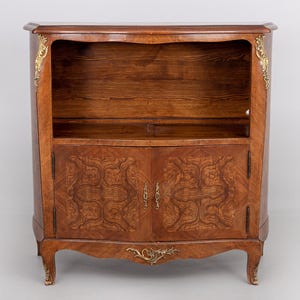 Puede incluir: Un mueble de madera con una parte superior curvada y detalles ornamentados. El mueble tiene dos puertas con un diseño estampado y un estante encima. Acentos dorados adornan las esquinas y la base. El mueble es de color marrón cálido.