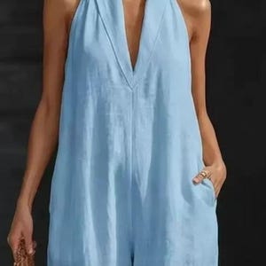 Op de afbeelding: Lichtblauwe halter jumpsuit met een V-hals en wijde pijpen. De jumpsuit heeft twee voorzakken en een losse pasvorm. De stof lijkt op lichtgewicht linnen, ideaal voor warm weer. De algehele stijl is casual en comfortabel.
