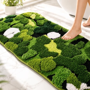May include: A rectangular bath mat featuring a high-pile, tufted texture in a multi-tonal pattern of forest green, lime green, black, and white. The rug has rounded corners and a dense, moss-like appearance with varying heights of soft fibers.