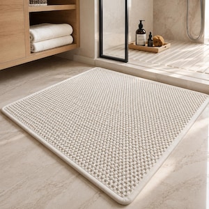 May include: A square, off-white bath mat featuring a raised, grid-like textured surface and a smooth, rounded border. The mat is constructed with a dense, woven fabric pattern that creates a uniform, tactile appearance across the entire top.