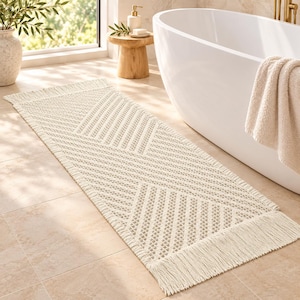 May include: A rectangular off-white woven runner rug featuring a geometric pattern of diagonal lines and a textured surface. The rug is finished with long, straight fringe detailing along both of its shorter ends, creating a clean look.
