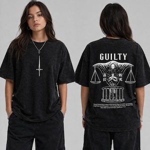 Puede incluir: Dos vistas de una camiseta negra. La parte delantera presenta un colgante de espada plateada. La parte trasera muestra la palabra "GUILTY" sobre un diseño de balanza y figura, con texto debajo.