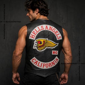 Op de afbeelding: Een zwart leren vest met een grote geborduurde patch op de achterkant. De patch toont de tekst HELLS ANGELS in het rood, een gevleugeld schedelembleem in geel, rood en wit, de letters MG en de tekst CALIFORNIA in het rood.