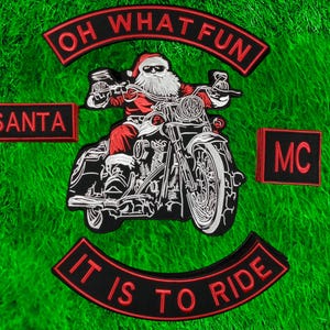 Puede incluir: Parche bordado con Papá Noel en una motocicleta. El diseño incluye las frases "OH WHAT FUN", "SANTA", "MC" y "IT IS TO RIDE" en letras rojas sobre un fondo negro. El parche está sobre un fondo verde.