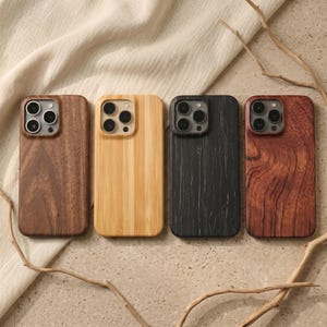 Puede incluir: Cuatro fundas de teléfono de madera en tonos marrones y negros. Las fundas tienen recortes para las lentes de la cámara y están hechas de diferentes vetas de madera. Las fundas están dispuestas en fila sobre un fondo neutro.