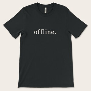 Op de afbeelding: Zwart T-shirt met het woord "offline." in het wit gedrukt. Het T-shirt met ronde hals is gemaakt van een zachte stof. De tekst is gecentreerd op de voorkant van het kledingstuk en biedt een minimalistisch ontwerp.