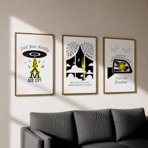 May include: Three framed art prints with gold frames hang above a gray sofa. The prints feature black and white graphics with yellow accents and text. One print says "Did You Really Beam Me Up?" Another says "Cause love's never lost when perspective is earned."