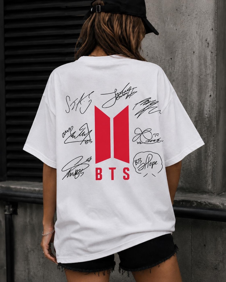 May include: White t-shirt featuring a red and white BTS logo with signatures. The shirt has a crew neck and short sleeves. The BTS logo is centered on the back of the shirt.