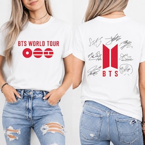 May include: White t-shirt featuring the text "BTS WORLD TOUR" in red on the front. The back of the shirt displays the BTS logo in red, along with signatures and the word "BTS".