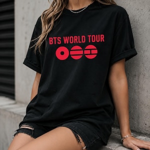 May include: Black t-shirt with the text "BTS WORLD TOUR" in red, along with a red graphic design. The shirt is a casual style, with rolled-up sleeves.