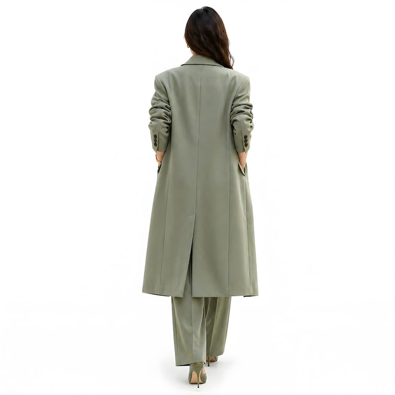 Pu&ograve; includere: Un cappotto lungo verde salvia e pantaloni abbinati. Il cappotto ha un design classico con revers a lancia, polsini con bottoni e tasche. I pantaloni sono a gamba larga. L'outfit &egrave; indossato con tacchi alti verdi.