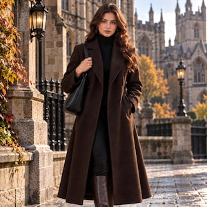 May include: A long, dark brown wool-blend coat with a structured collar and lapels, worn over a black turtleneck sweater. The coat features a flared silhouette, long sleeves, and side pockets, paired with a black shoulder bag and dark brown boots.