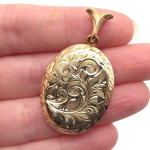May include: Oval gold-colored locket with intricate floral and scroll engraving. The locket has a decorative bail and a detailed border. A classic piece of jewelry, perfect for holding a small photo or keepsake.
