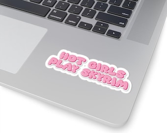 May include: A pink sticker with the text "HOT GIRLS PLAY SKYRIM" in a bubble font, placed on a laptop. The sticker has a white border and is positioned near the keyboard.