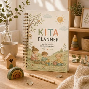 Könnte beinhalten: Ein spiralgebundenes Kita-Planer-Notizbuch mit einer Illustration in sanften Farben, die drei Kinder beim Spielen auf einer Wiese mit Baum, Sonne und Wolken zeigt. Das Cover trägt den Text KITA PLANNER sowie Mit Herz planen. Mit Freude begleiten.