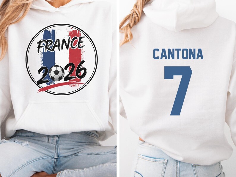 Puede incluir: Sudadera con capucha blanca con un gr&aacute;fico frontal con la palabra "FRANCE" encima de un bal&oacute;n de f&uacute;tbol y el a&ntilde;o "2026" en negro. La parte trasera de la sudadera muestra el nombre "CANTONA" y el n&uacute;mero "7" en azul.