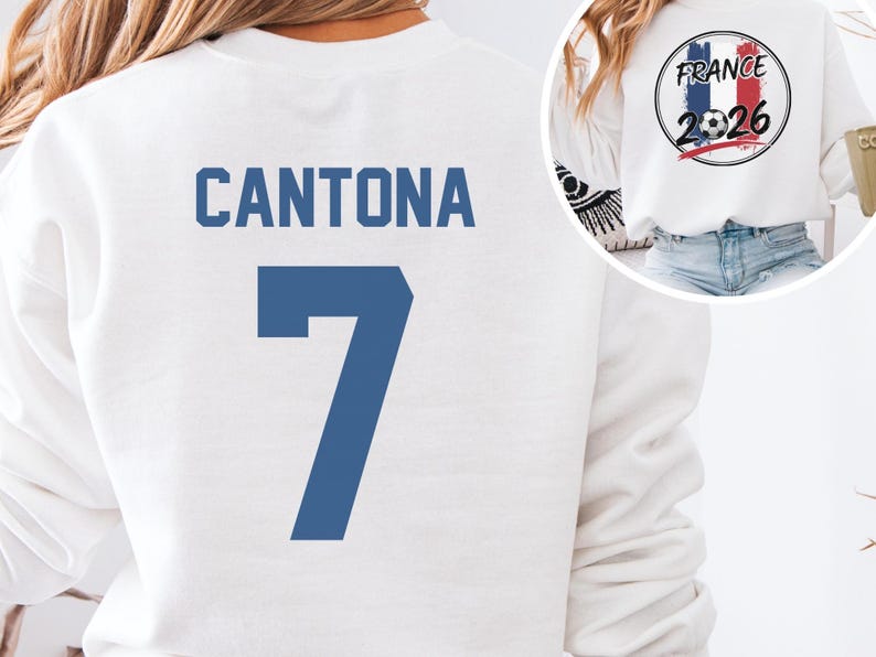 White short-sleeve t-shirt featuring CANTONA 7 printed in classic blue on the back. A small inset circle shows the front graphic with a vintage France flag, a soccer ball, and the text FRANCE 2026.