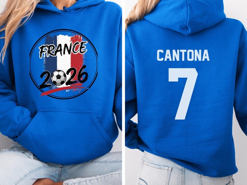 Puede incluir: Una sudadera con capucha azul real con un gr&aacute;fico de la bandera francesa, un bal&oacute;n de f&uacute;tbol y el texto "FRANCE 2026". La parte trasera de la sudadera muestra el nombre "CANTONA" y el n&uacute;mero "7" en blanco. La sudadera tiene un bolsillo delantero y una capucha.