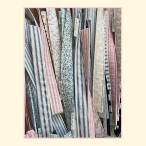 May include: A collection of long, narrow fabric strips featuring various patterns including blue and white stripes, pink and white stripes, floral prints, and solid colors. Each strip has a small white tag labeled "plony projects" attached.