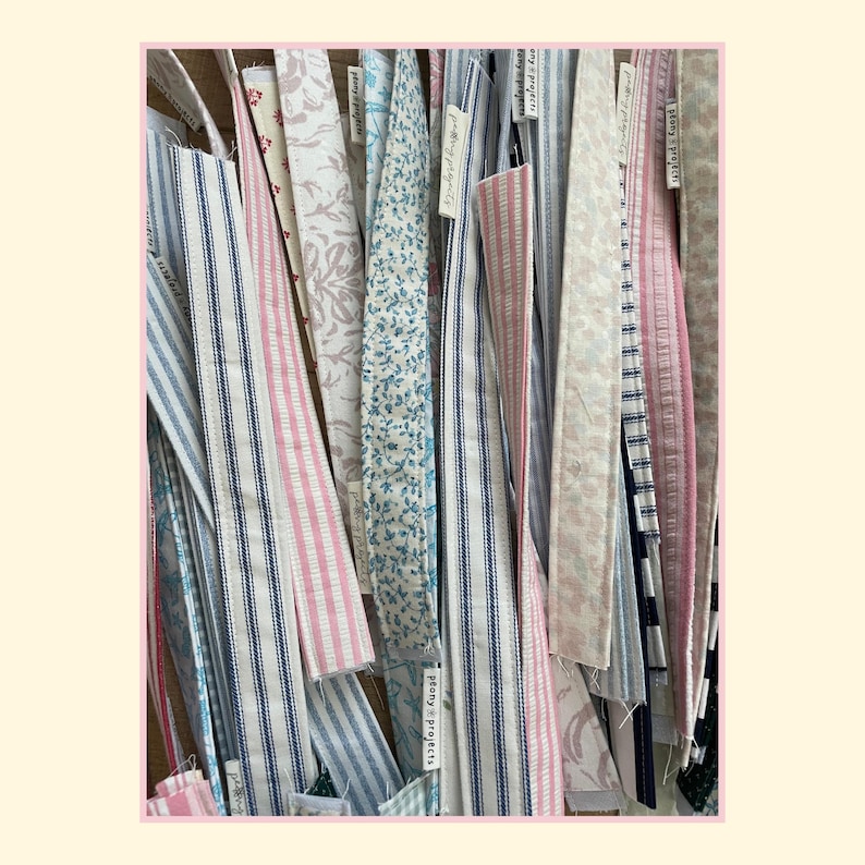 May include: A collection of long, narrow fabric strips featuring various patterns including blue and white stripes, pink and white stripes, floral prints, and solid colors. Each strip has a small white tag labeled "plony projects" attached.