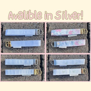 May include: Eight fabric wristlet keychains with metal hardware, featuring various patterns including blue stripes, gingham, and floral prints. Each keychain has a small white tag labeled peony projects. The text Avalible in Silver! is at the top.