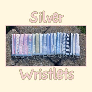 May include: A collection of fabric wristlets featuring various patterns including stripes, florals, gingham, and solid colors. Each wristlet is attached to a silver-toned metal hardware clasp and ring. The text Silver Wristlets is displayed.