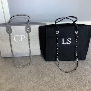 以下が含まれることがあります： 2つのトートバッグ。1つは白のイニシャル「CP」が入ったライトグレー、もう1つは白の「LS」が入った黒です。どちらもシルバーチェーンのストラップとグレーのハンドルが付いています。