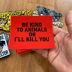 May include: A red square patch with the text "BE KIND TO ANIMALS OR I'LL KILL YOU" in black. Other patches with animal graphics are visible in the background.