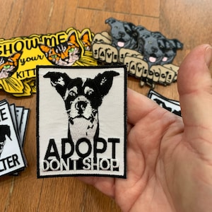 May include: White iron-on patch with a black and white dog illustration and the text "Adopt Don't Shop".