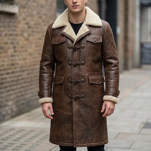 May include: A long brown leather coat featuring a cream-coloured shearling collar and lining. The coat includes four toggle closures down the front, two chest pockets with flaps, and two lower pockets with flaps, with shearling cuffs at the sleeves.