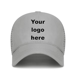 May include: A light gray baseball cap with the text "Your logo here" in black. The cap has a curved brim and small ventilation holes on the sides. The hat is made of a smooth material.