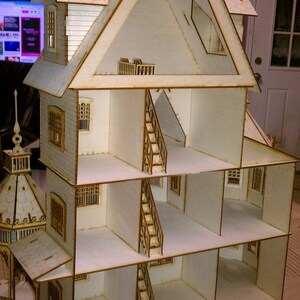 以下が含まれることがあります： 4階建ての白い木製のドールハウス。各階にバルコニーと階段があり、屋根は切妻屋根で、側面には小さな塔があります。