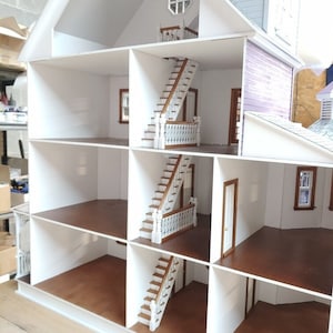 May include: A white dollhouse with four levels and three staircases. The dollhouse has a brown wooden floor and white walls. The dollhouse is open and the interior is visible.