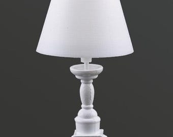 Könnte beinhalten: Eine kleine, weiße Tischlampe mit klassischem Design. Die Lampe hat einen konischen Lampenschirm und einen dekorativen Sockel. Der Sockel hat eine Sockelform mit Zierdetails. Die Lampe besteht aus einem festen, undurchsichtigen Material.