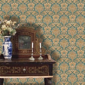 May include: A teal and gold damask wallpaper pattern forms the backdrop for a vintage wooden table. The table holds a decorative mirror, two silver candle holders with lit candles, and a blue and white vase with flowers.
