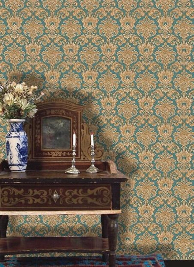 May include: A teal and gold damask wallpaper pattern forms the backdrop for a vintage wooden table. The table holds a decorative mirror, two silver candle holders with lit candles, and a blue and white vase with flowers.