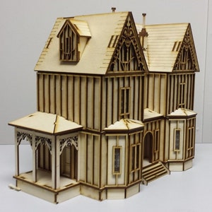 May include: A wooden model of a two-story house with a porch, intricate details, and a gabled roof. The model is made of light brown wood and has a white background.