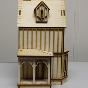 May include: A wooden model of a two-story house with a porch and a dormer window. The model is made of light brown wood and has a simple design.