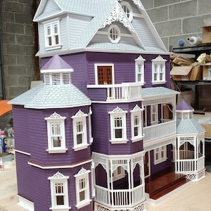 May include: A purple dollhouse with white trim and a gray roof. The dollhouse has multiple levels and balconies. The dollhouse is decorated with intricate details, including a cupola and gingerbread trim.