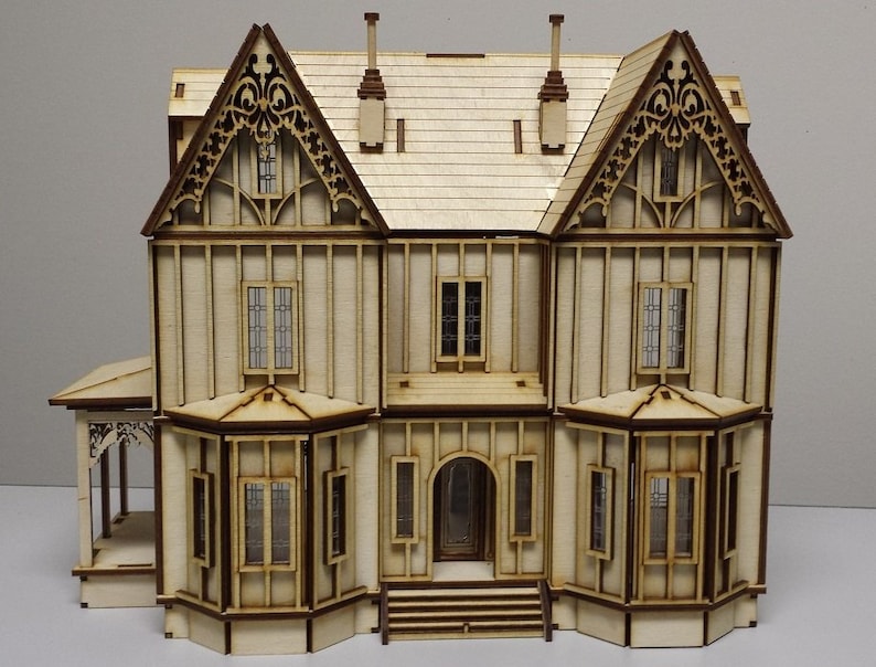 May include: A wooden model of a two-story house with a gabled roof, intricate details, and multiple windows. The house is painted in a light wood color and has a brown trim.